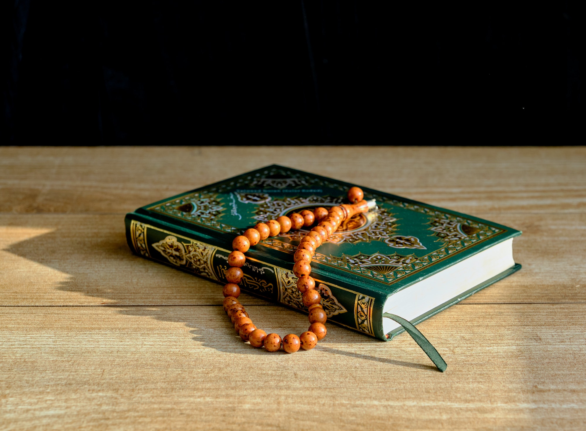A green and gilded book of Quran and a rosary